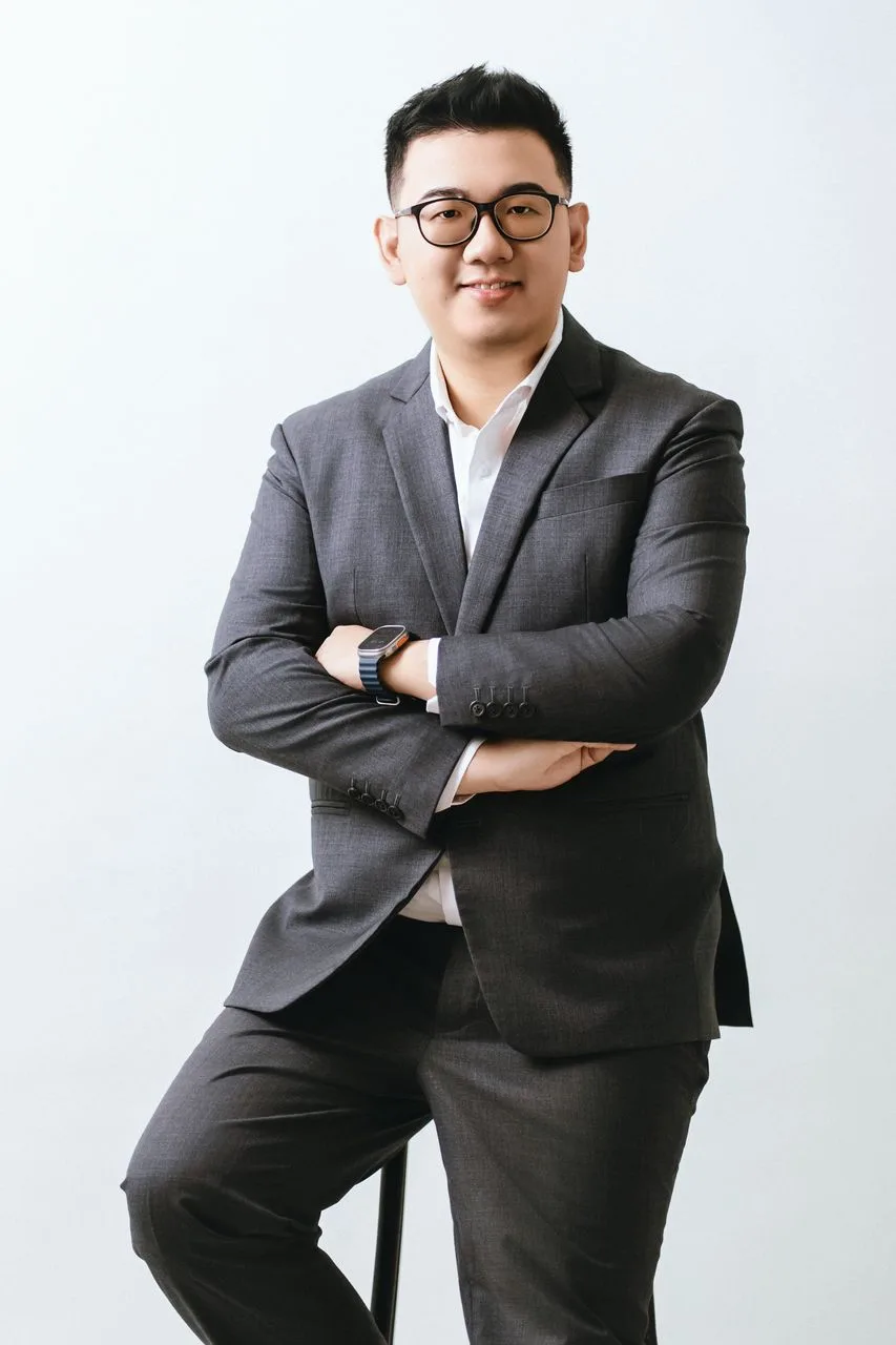 Man in gray suit posing with arms crossed. Professional headshot.